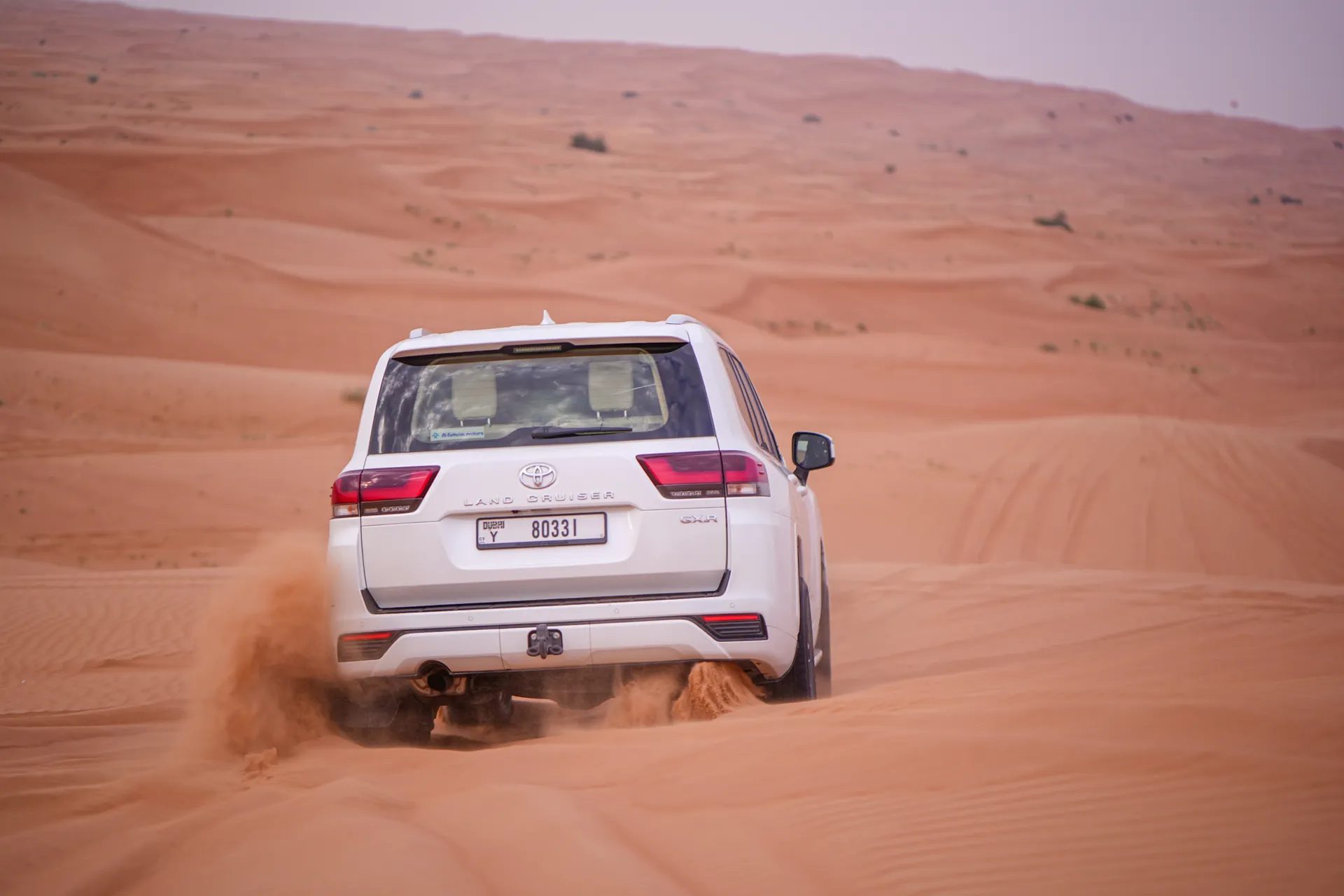 White Land Cruiser driving over desert dunes in Dubai